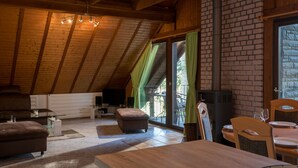 Une pièce confortable de style loft, avec un plafond en bois, une cheminée, un coin repas avec une table et des chaises, et une grande fenêtre avec des rideaux.