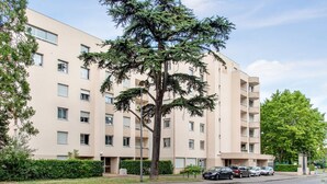 A multi-story residential building with a beige facade, multiple balconies, and a parking area with several cars. - Appartement Mansana - Welkeys (Caluire-et-Cuire)