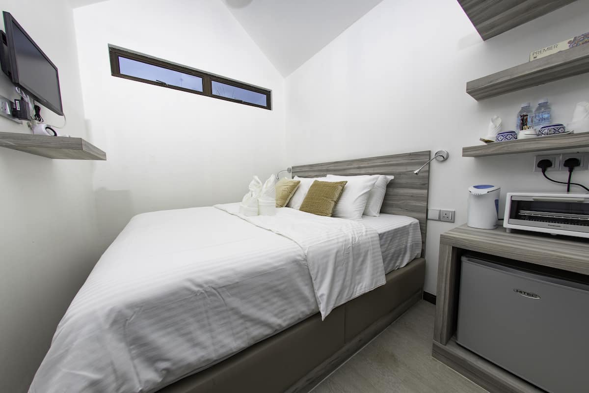 Une chambre d’hôtel compacte comprenant un lit, une petite kitchenette, une fenêtre et un téléviseur fixé au mur.