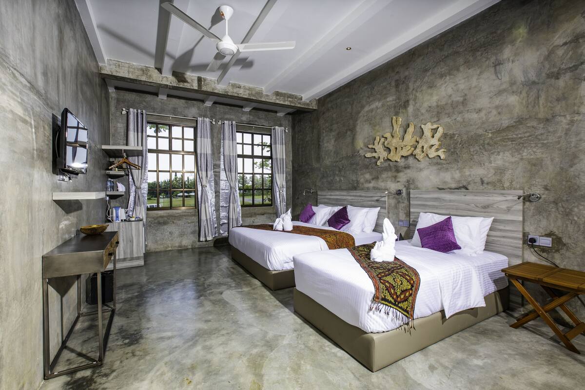 Une chambre d’hôtel moderne équipée de deux lits, d’une télévision, d’un bureau et d’une grande fenêtre.