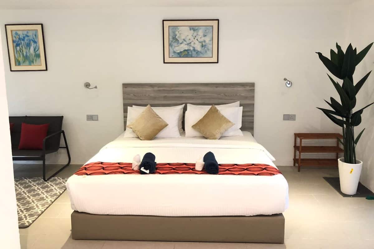 Une chambre d’hôtel moderne avec un grand lit, deux oreillers, une tête de lit en bois, une couverture à rayures rouges et blanches, une plante en pot et des œuvres d’art accrochées aux murs.