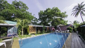 Une piscine dotée d’une terrasse en bois, entourée d’une végétation luxuriante et de palmiers.