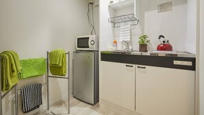 A compact kitchen with a microwave, refrigerator, and a kettle on the counter. There are towels hanging on a rack and a small potted plant on the counter.