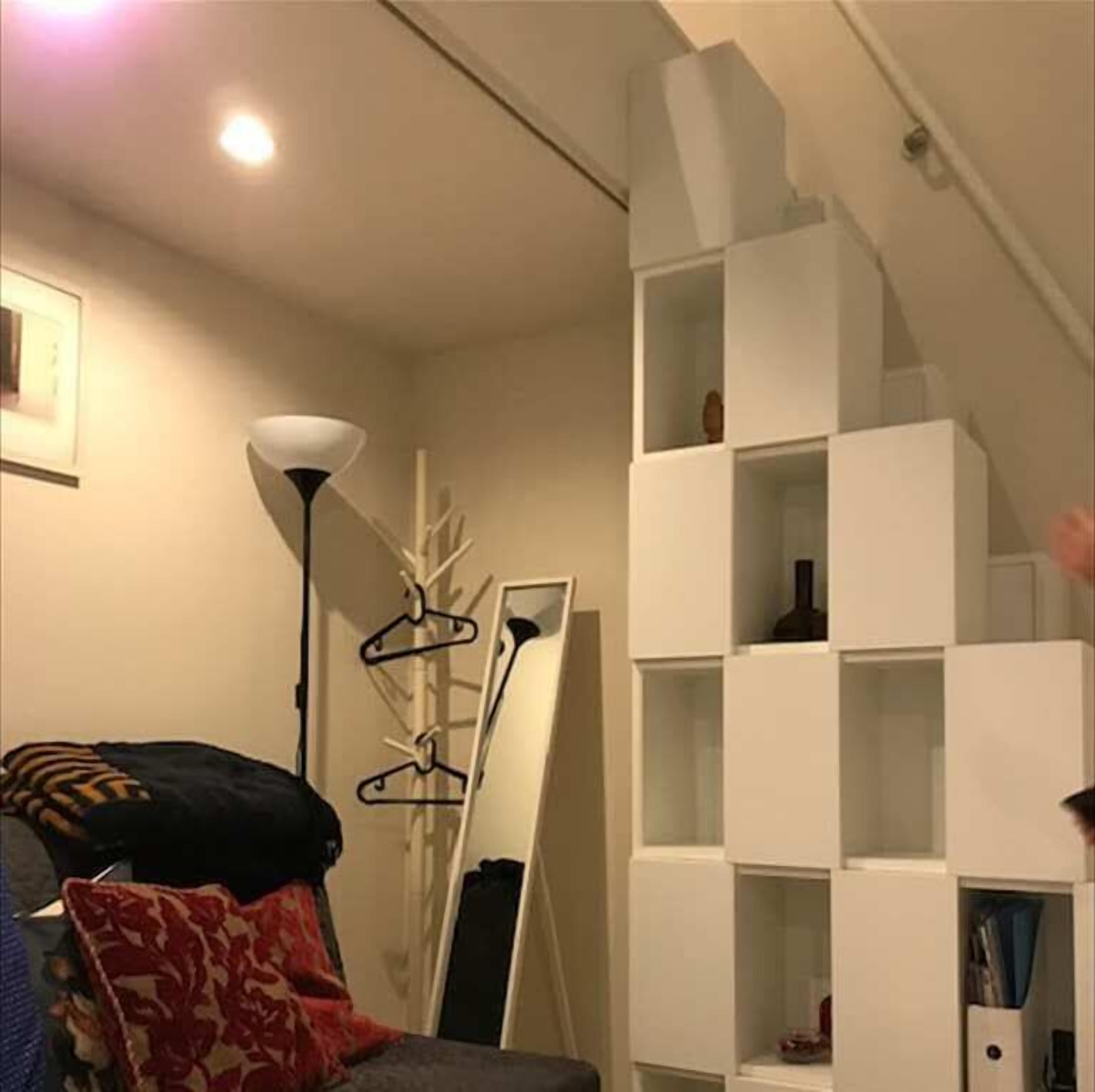 A room with a white shelving unit against the wall, a floor lamp, and a bed with a patterned blanket.