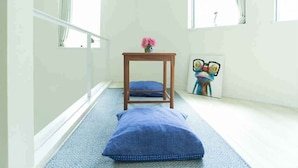 A room with a blue patterned rug, a wooden chair with a cushion, a small table with a vase of flowers, and a colorful artwork on the wall.