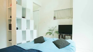 A bedroom with a bed, a TV, a plant, and built-in shelving.