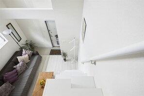 A modern interior with a staircase leading to an upper level, a sofa with patterned cushions, a small table with a bowl of fruit, and a potted plant. - Just 9 minutes from the famous Shibuya Crossing and a stone's throw from Ebisu, Nakameguro, and Daikanyama! A stylish new room with a loft is now open. (Shibuyaku Higashi)