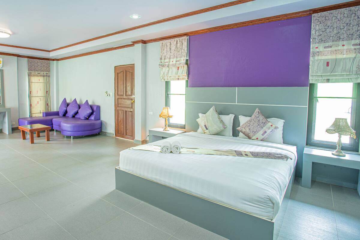 Ein Schlafzimmer mit einem Bett, einem violetten Sofa, einem Schreibtisch und einem Sessel.