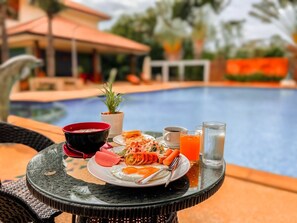 A dining table with a meal, a glass of orange juice, and a glass of water by a poolside. - Muak Lek Forest Resort (Muak Lek)