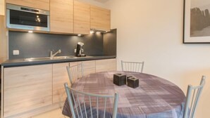 A modern kitchen with wooden cabinets, a built-in oven, and a coffee machine. There is a round dining table with chairs and two decorative blocks on it. - Deauville II 010 with parking by Interhome (Bredene)