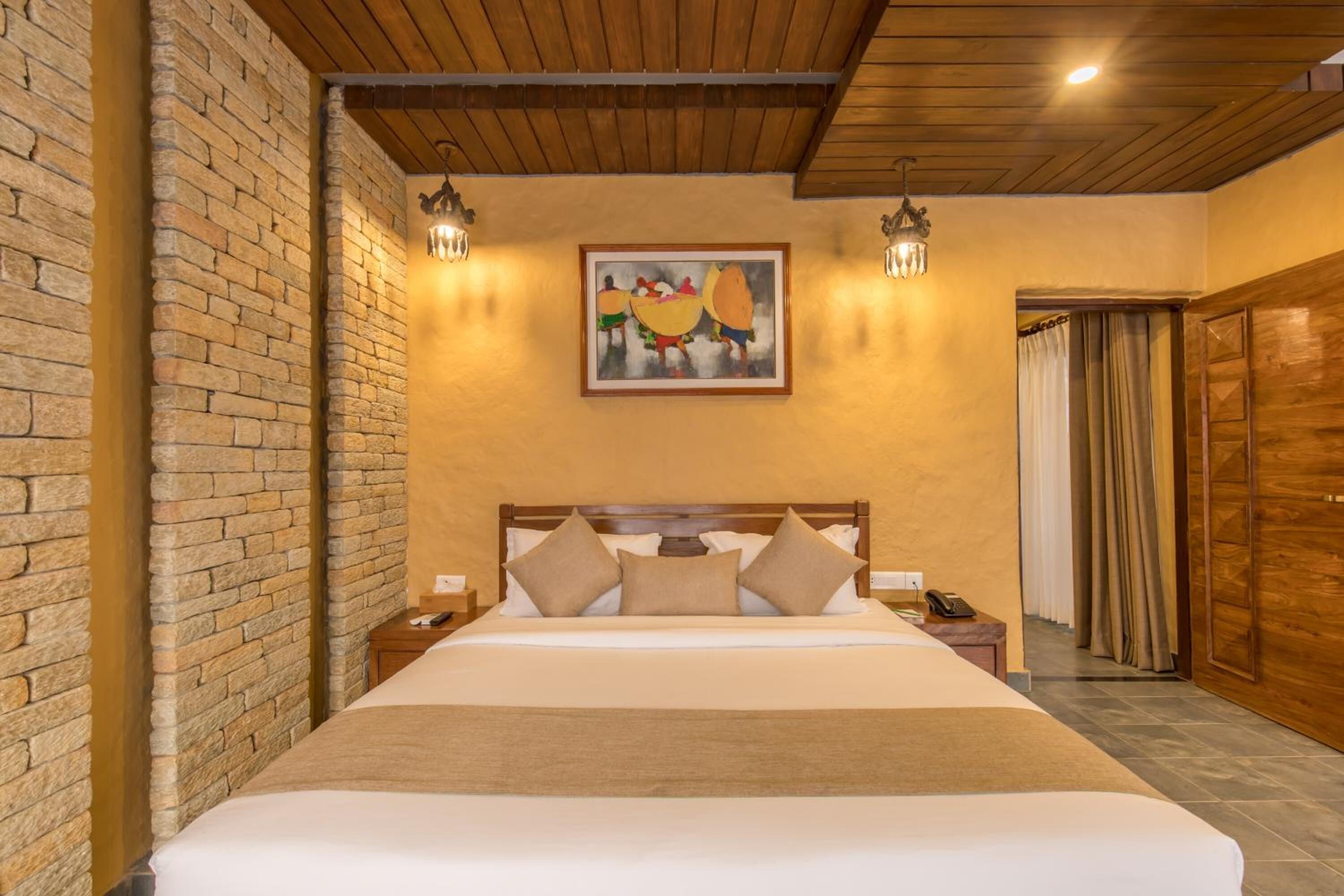 A hotel room with a large bed, wooden headboard, brick walls, and a painting on the wall.