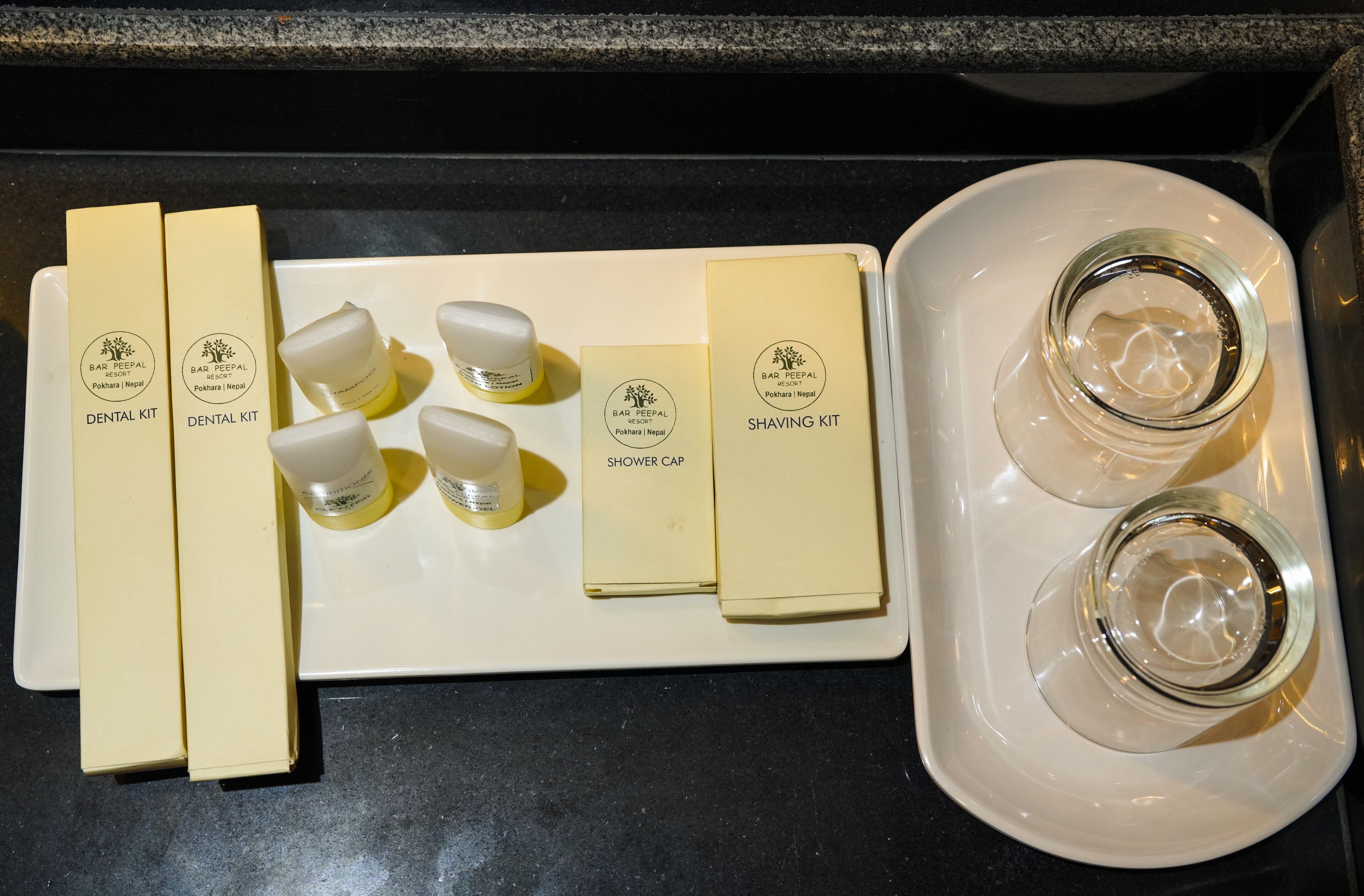 A tray with a dental kit, shaving kit, and two empty glasses on a kitchen counter.
