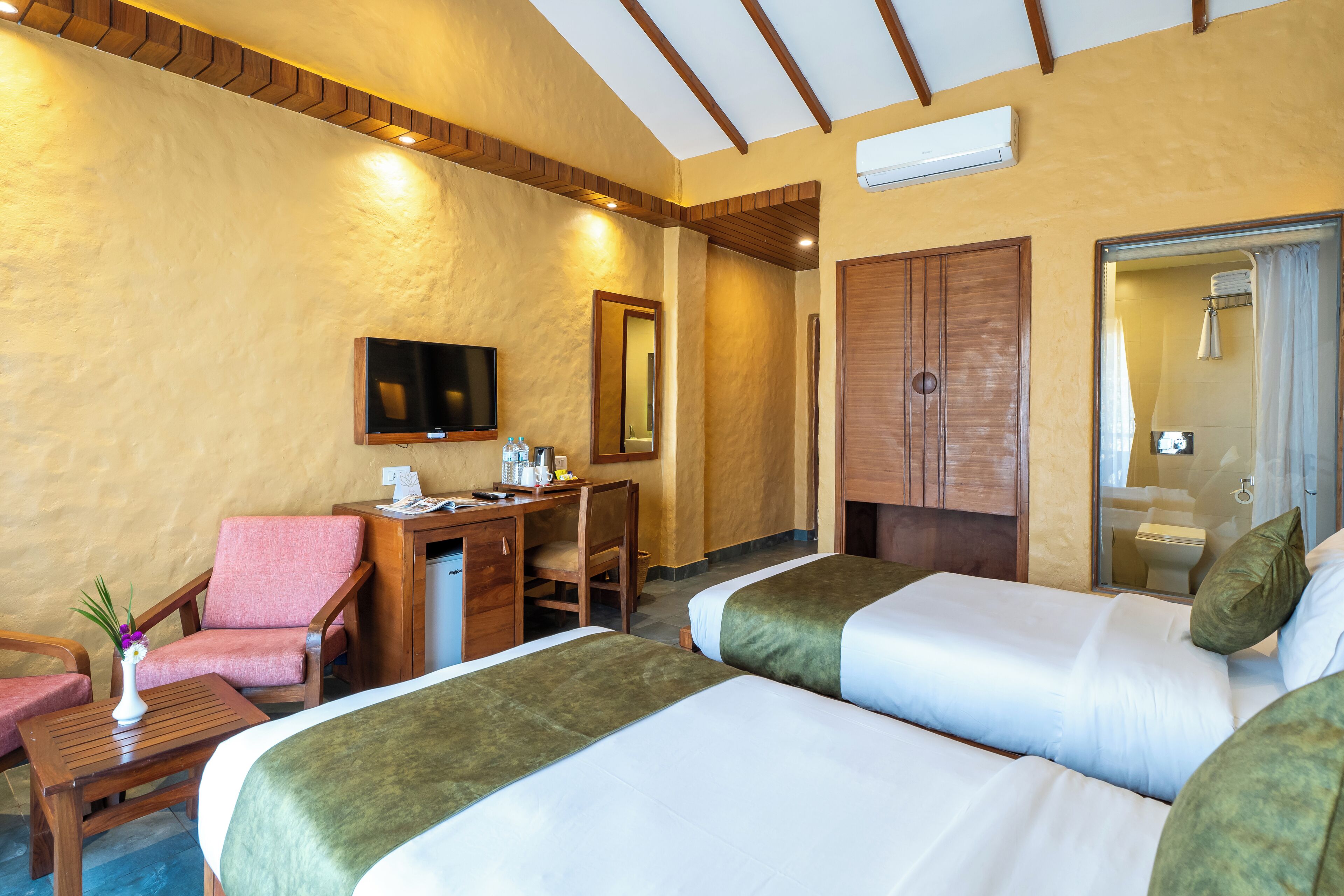 A hotel room with two beds, a desk with a chair, a TV, and a shower area.