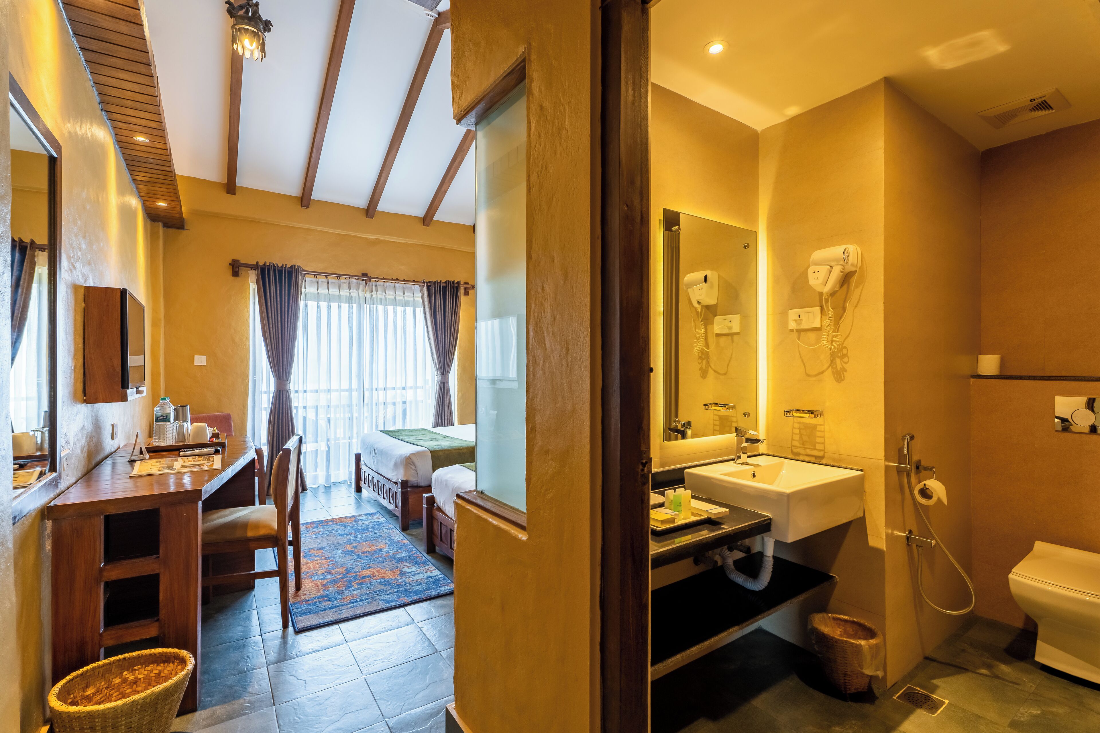 A hotel room with a wooden desk, a bed, a bathroom with a sink and toilet, and a mirror.