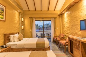 A hotel room with a bed, a desk, a chair, a TV, and a balcony with a view of a mountain and a traditional building. - Bar Peepal Resort (Pokhara)