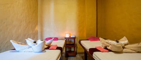 Una habitación con dos camas, cada una con toallas y almohadas, y una mesita con una lámpara en el centro.
