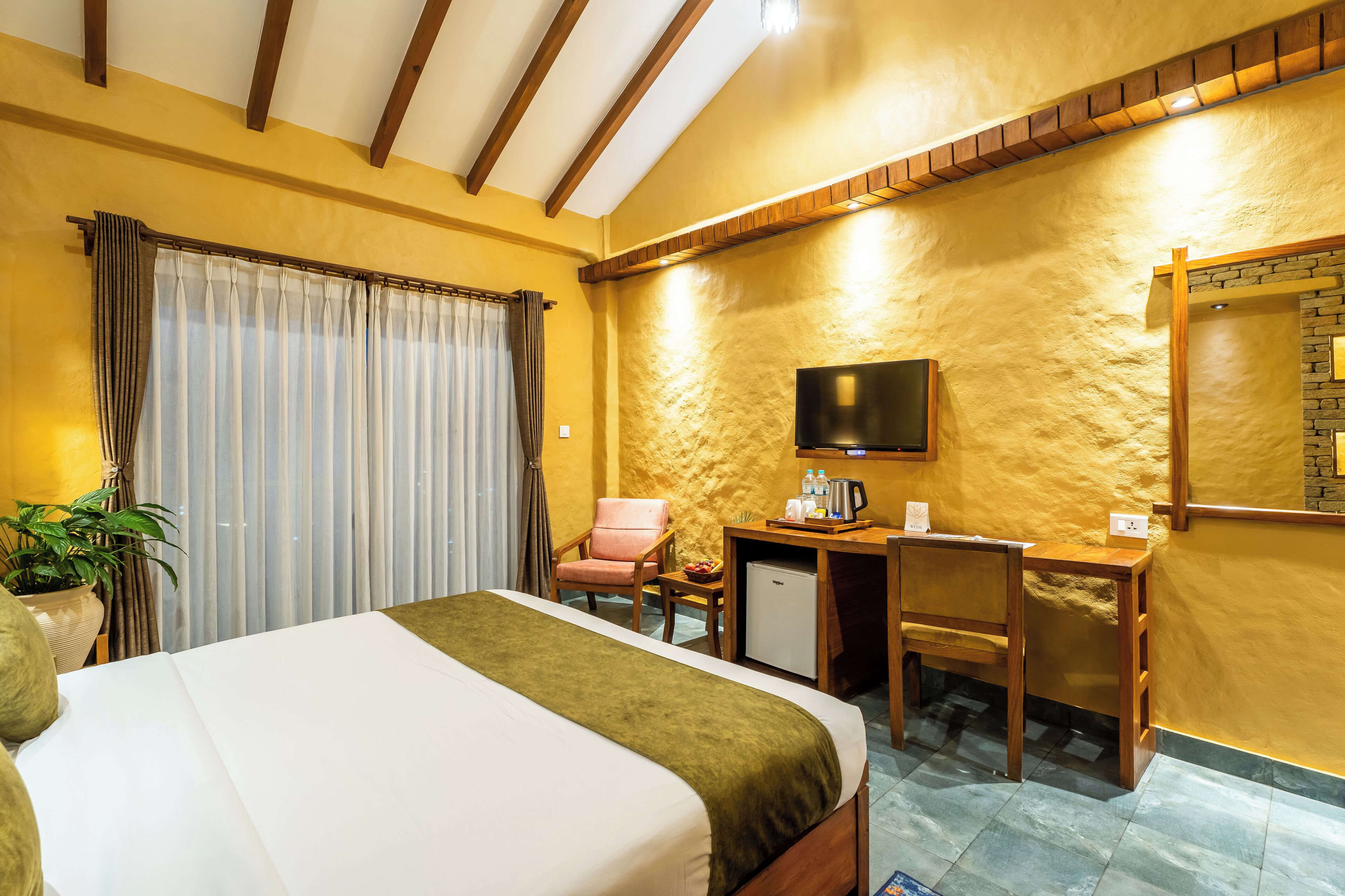 A hotel room with a bed, a desk, a chair, a television, and a small refrigerator.