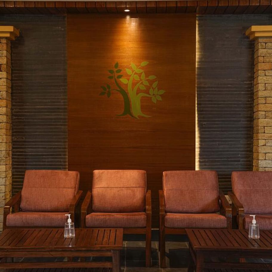 A lobby with a wooden reception desk, three cushioned chairs, and a wall with a tree mural.