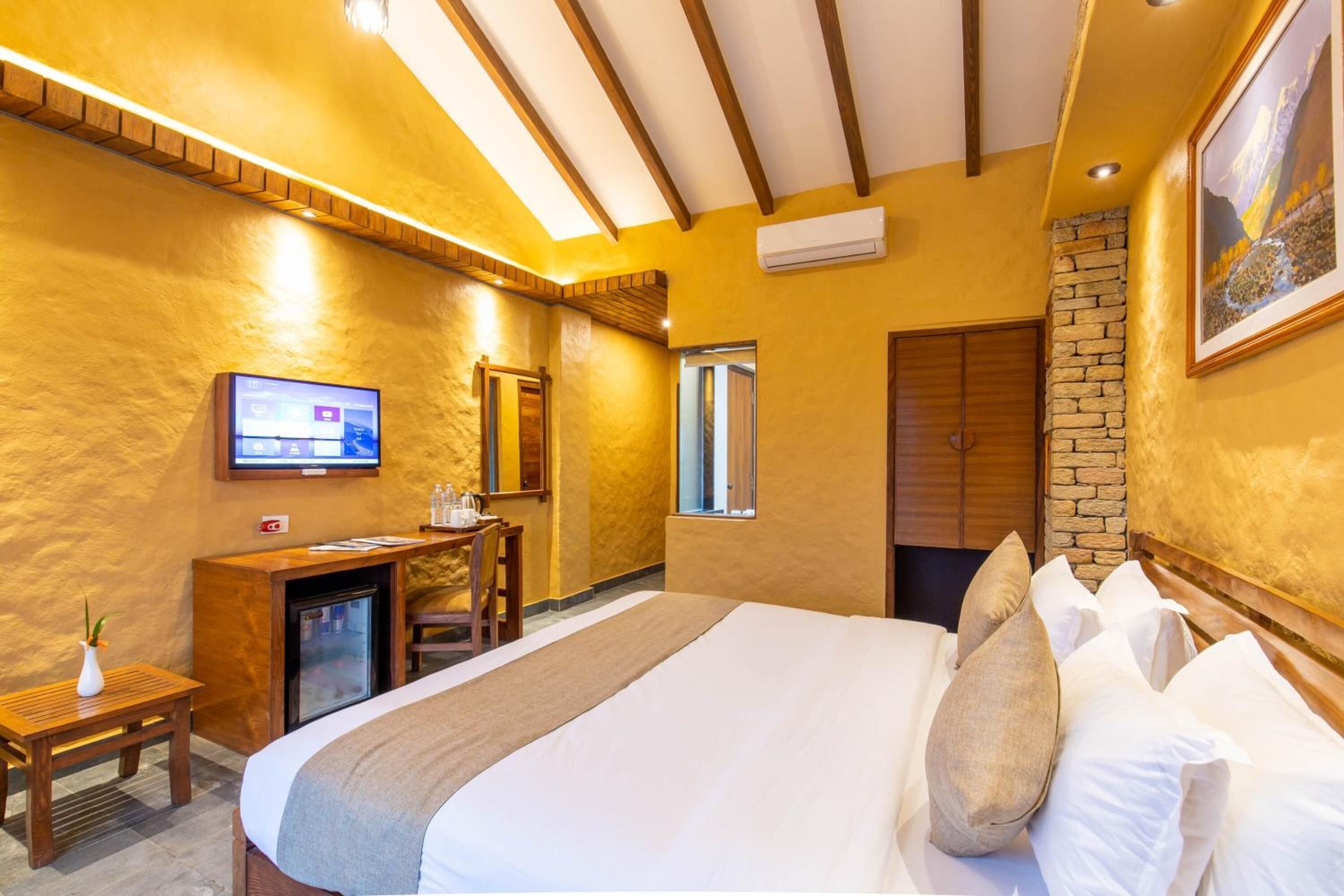Una habitación de hotel con una cama, un escritorio con computadora, un televisor y una pared de piedra.