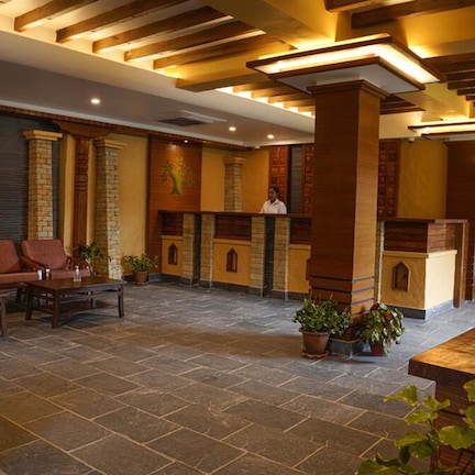 A lobby with stone flooring, wooden furniture, and potted plants.