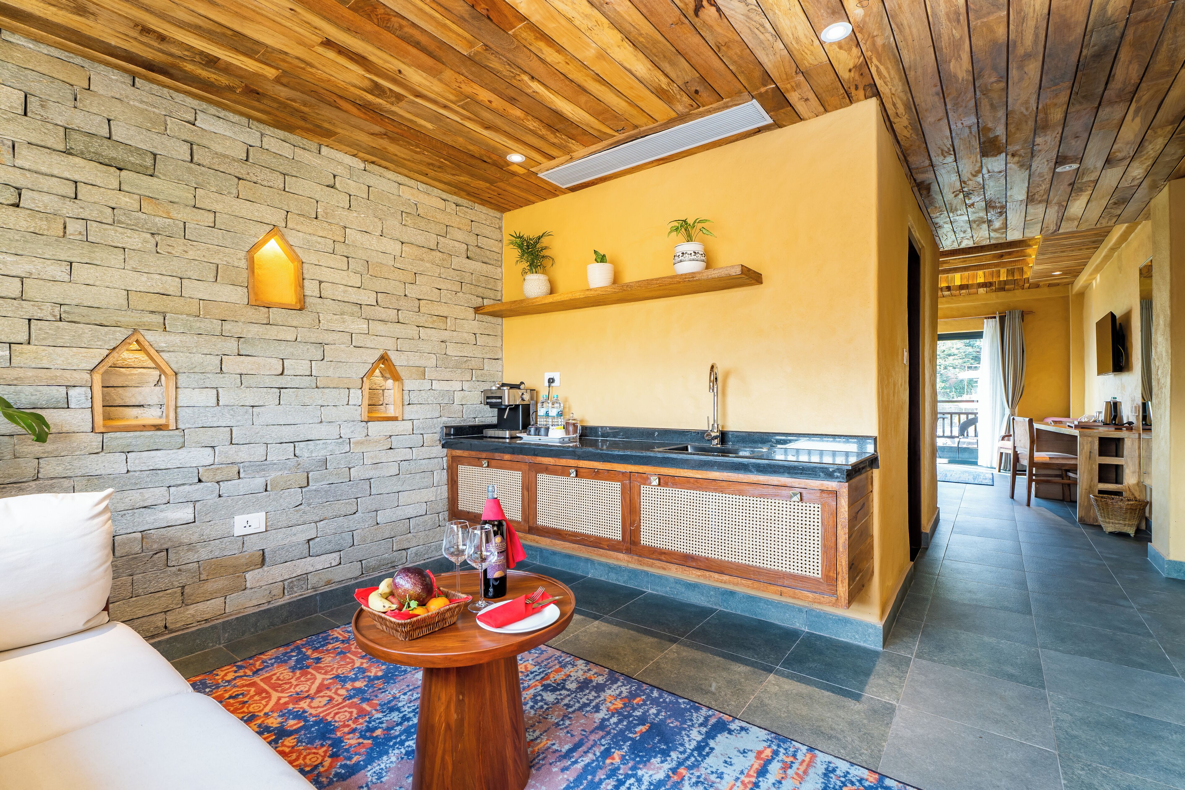 A cozy interior with a stone wall, wooden ceiling, and a bar area with plants.