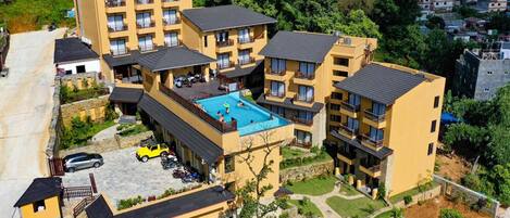 Um hotel com vários andares e piscina no terraço, rodeado por vegetação exuberante e uma paisagem montanhosa.