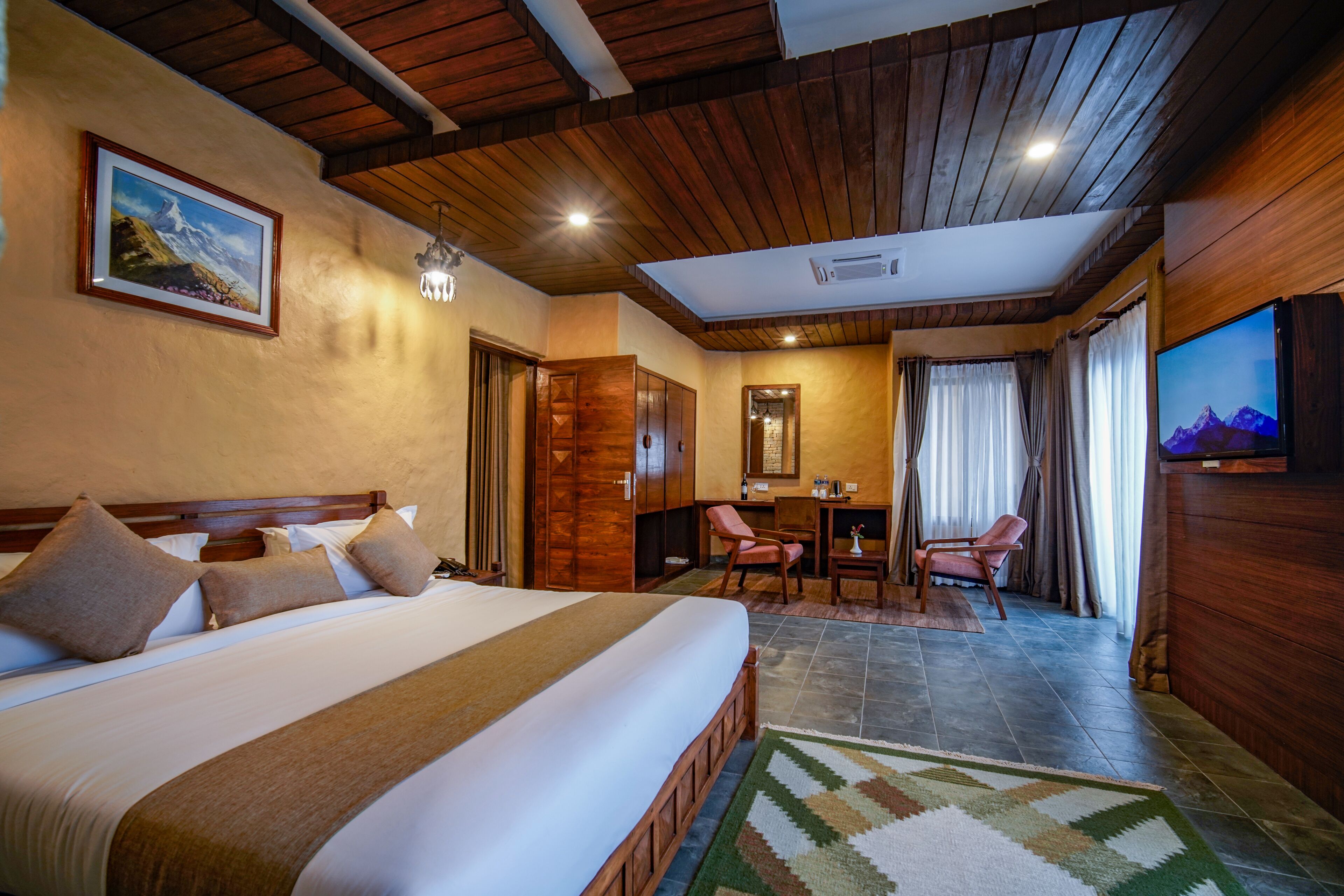 Habitación de hotel con una cama grande, techo de madera, un cuadro, un escritorio, una silla y un televisor.