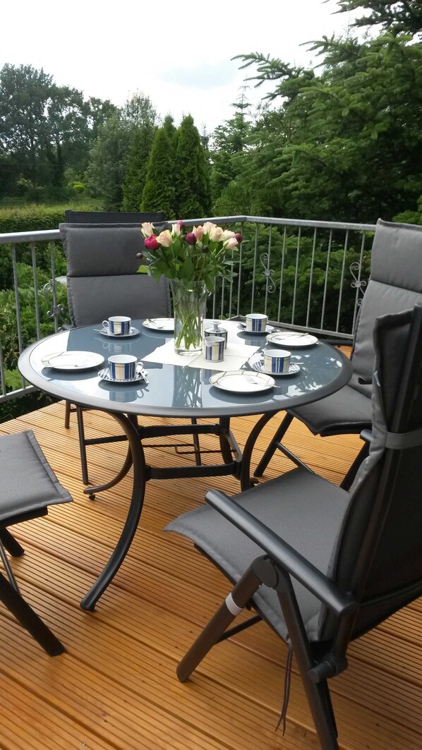 A round glass table with four chairs, a vase with flowers, and a metal railing.