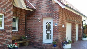 A brick building with a white door, a bench, and potted plants. - Ferienwohnung 3 - Ferienwohnung Haus Bikker (Ihlow)