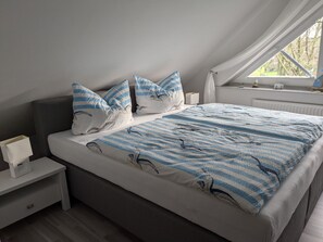 A bedroom with a bed, pillows, bedside tables, and a window.