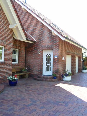 A brick building with a white door, a bench, and potted plants. - Ferienwohnung 3 - Ferienwohnung Haus Bikker (Ihlow)