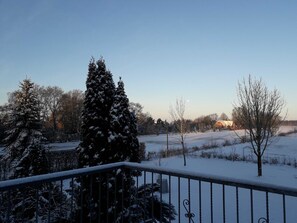 A snowy landscape with a clear sky, a snow-covered tree, and a distant building. - Ferienwohnung 3 - Ferienwohnung Haus Bikker (Ihlow)