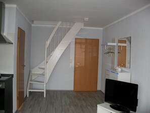 A room with a staircase, a wooden door, a white cabinet, a television, and a mirror on the wall.