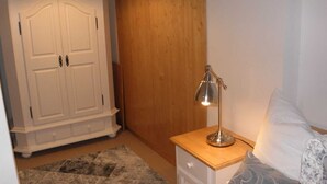 A bedroom with a wooden wardrobe, a bedside table with a lamp, and a patterned rug. - Sleep well apartment, Germany (Görlitz)