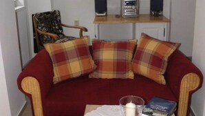 A cozy living room with a red sofa, plaid cushions, a coffee table with a candle, books, and a glass of water. - Sleep well apartment, Germany (Görlitz)