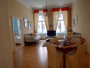A cozy living room with a sofa, a TV, a dining table with chairs, and a window with curtains.