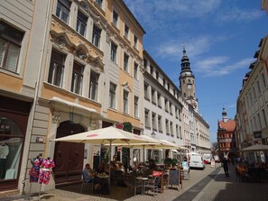 A street with outdoor seating, a clock tower, and historic buildings.