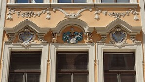 Fachada de edificio con tres ventanas grandes, detalles arquitectónicos ornamentales y elementos decorativos.