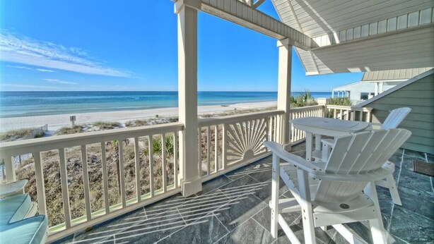 A covered outdoor area with a view of the beach, white chairs, and a table.