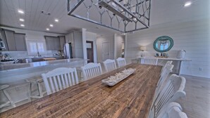 A spacious kitchen with white cabinetry, a central island, and a dining area with a wooden table and white chairs.