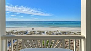 A beach view from a balcony with a white railing, sandy beach, and ocean.