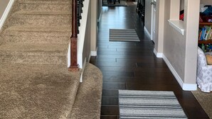 Un hall d’entrée spacieux avec un escalier recouvert de moquette, un tapis au pied de l’escalier et une bibliothèque sur le côté droit.