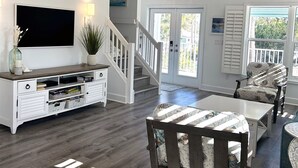 Ein geräumiges Wohnzimmer mit Flachbildfernseher, weißem Unterhaltungsmöbel und einer Treppe, die auf einen Balkon führt.