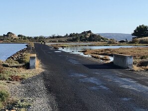A rural road with a bridge over a river, surrounded by natural landscapes and hills.