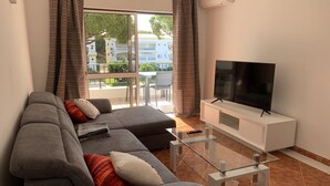 A modern living room with a grey sofa, a flat-screen TV on a white cabinet, and a glass coffee table. - Pinhal Do Golf: Superb 2-bedroom apartment, renovated in 2020 near Marina (Quarteira)