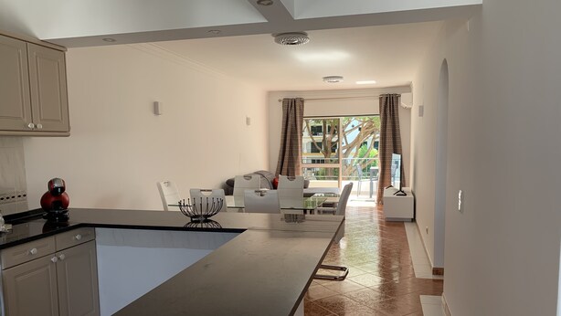 A modern kitchen with a large island, white cabinetry, and a dining area with a glass table and white chairs. - Pinhal Do Golf: Superb 2-bedroom apartment, renovated in 2020 near Marina (Quarteira)
