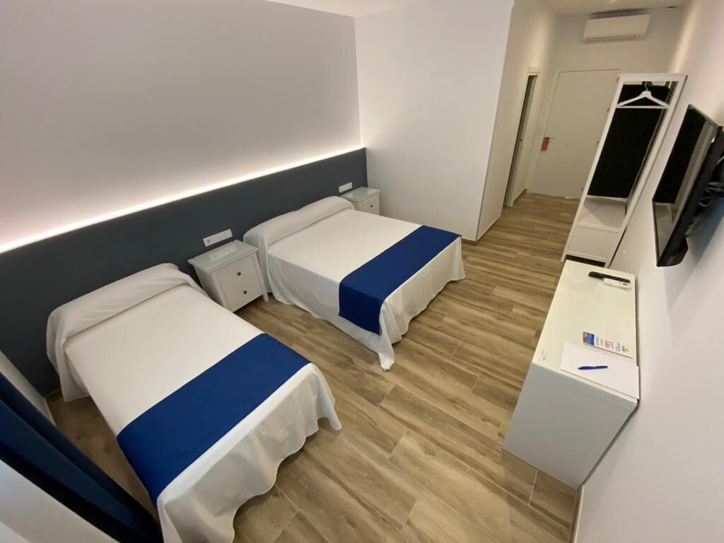 A hotel room with two beds, a desk, and a wardrobe.