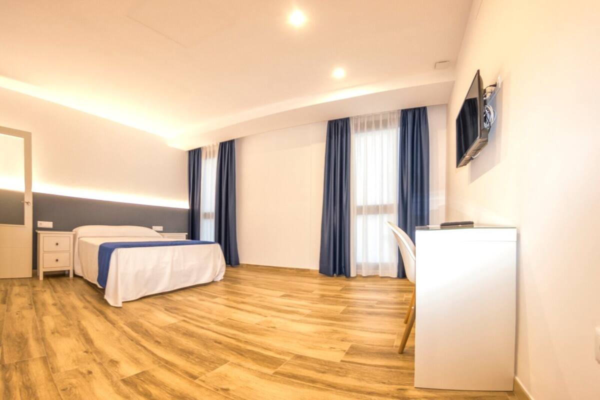 A hotel room with a bed, a desk, a chair, a TV, and a window with curtains.