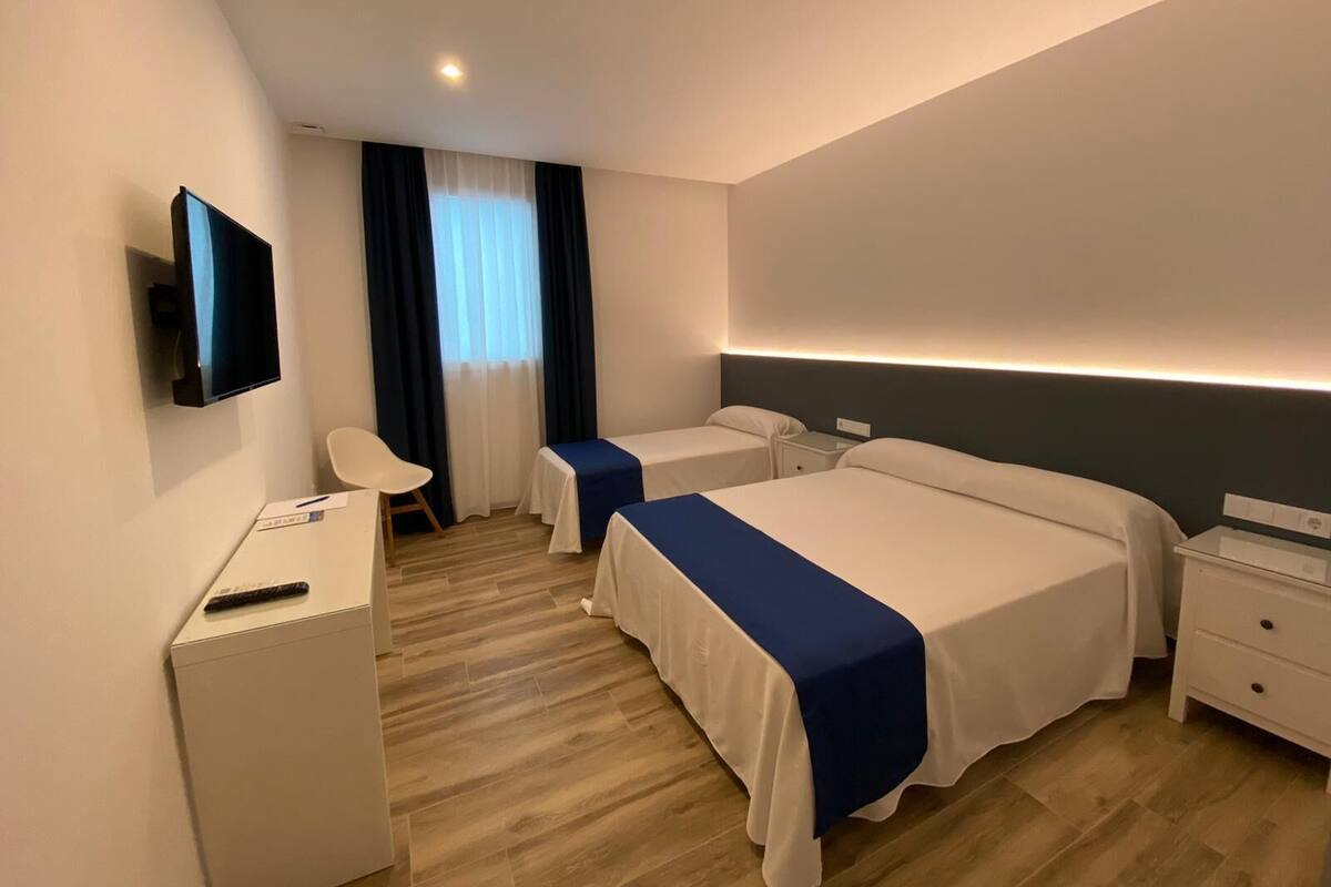 A hotel room with two beds, a desk, a chair, a TV, and a window with curtains.