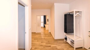 Un couloir avec un plancher en bois, une porte blanche et une armoire blanche dotée d’une étagère.